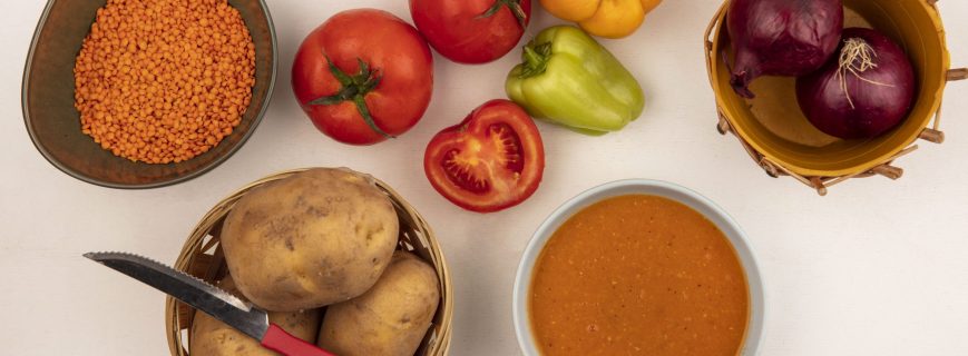 top view of nutritious lentil soup on a bowl with red onions on a bucket with potatoes on a bucket with knife with peppers and tomatoes isolated on a white background top view of nutritious lentil soup on a bowl with red onions on a bucket with potatoes on a bucket with knife with peppers and tomatoes isolated on a white background